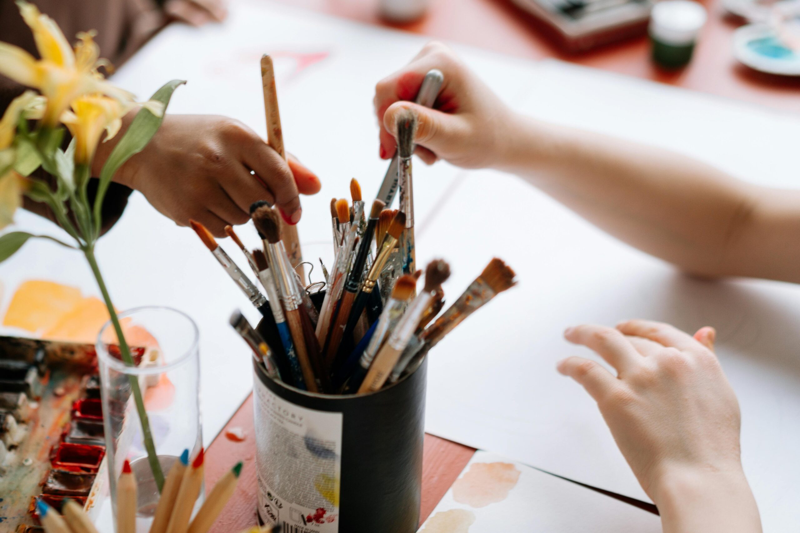 Hands reaching for paintbrushes in an artistic indoor setting.